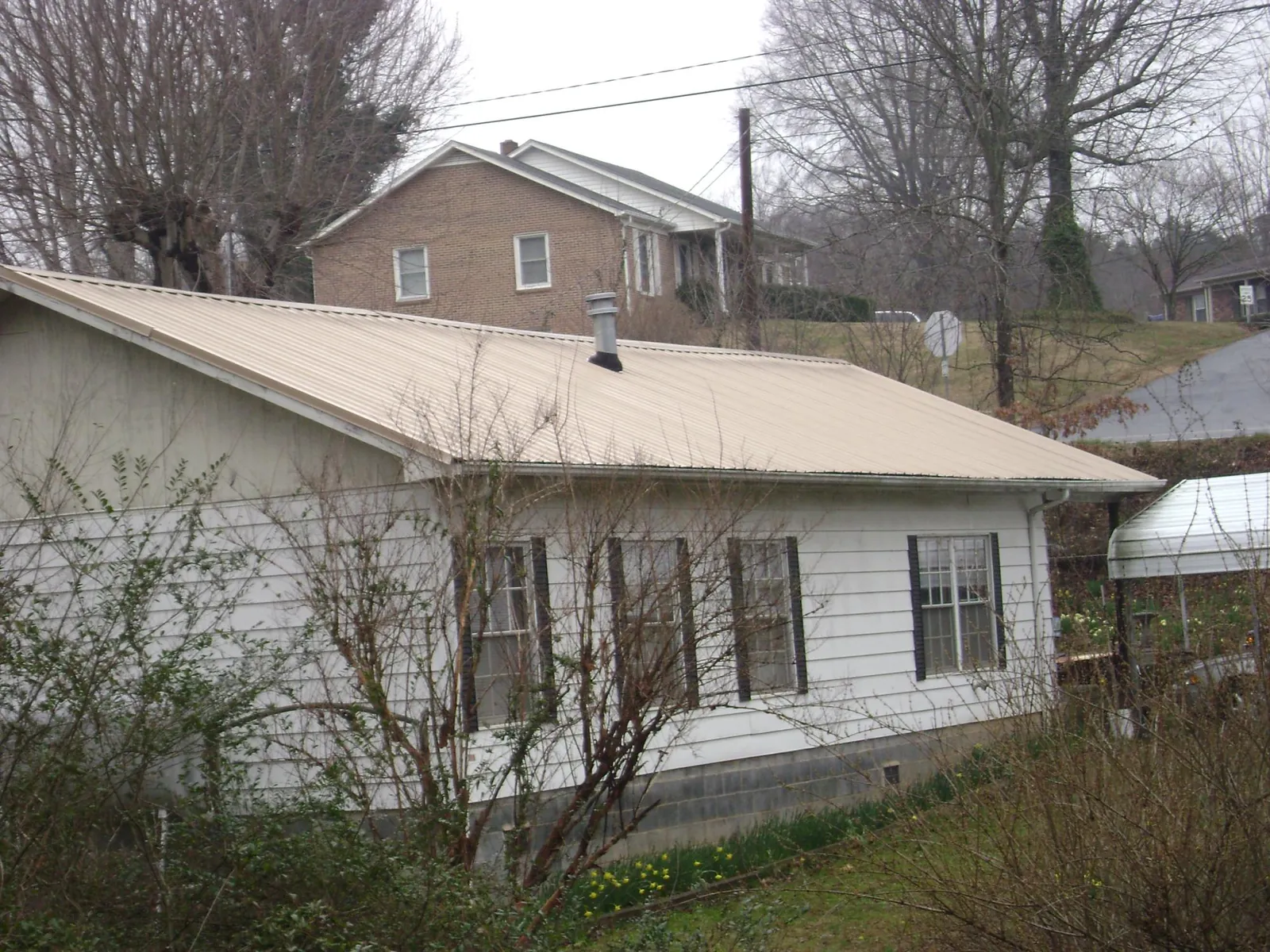 Tan metal roof on a white sided house set into a hillside — Commercial Roofing by Roofing Brothers in Bradford