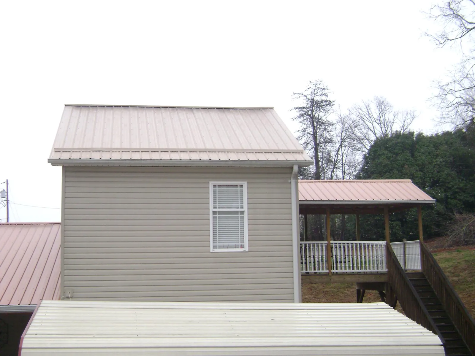 Tan metal roofs on a two story addition and attached porch, from a Roof Replacement job in Bradford